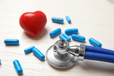 Stethoscope, red heart and pills on wooden background. Cardiology concept