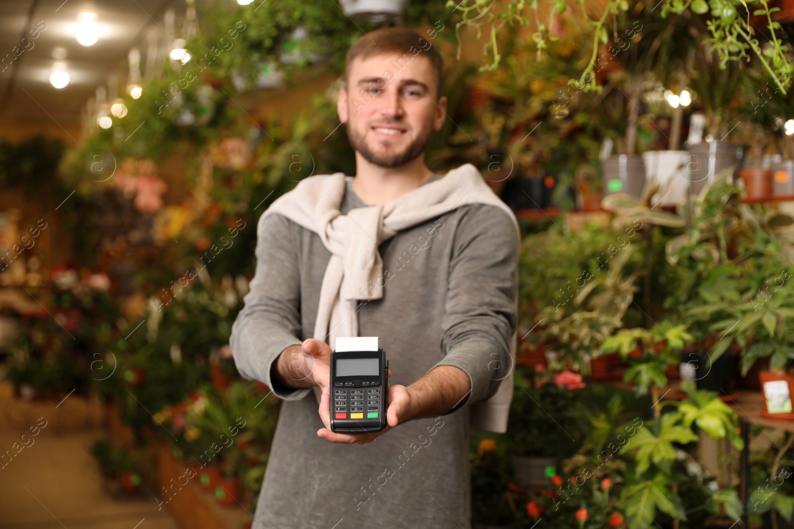 Photo of Smiling seller holding payment terminal in floral shop