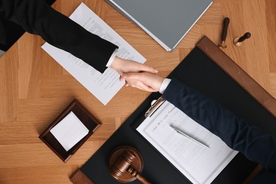 Photo of Notary shaking hands with client at wooden table, top view