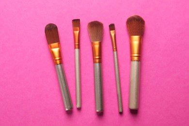 Photo of Different makeup brushes on pink background, flat lay