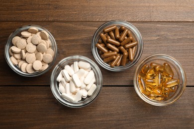 Different dietary supplements in glass bowls on wooden table, flat lay