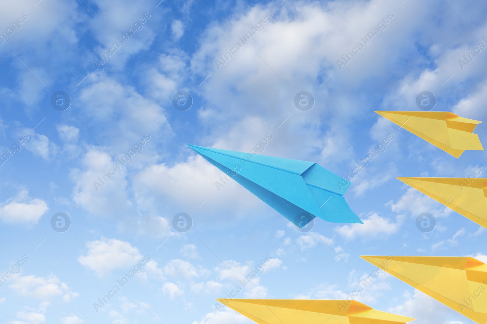 Image of Light blue and yellow paper planes flying in sky with clouds