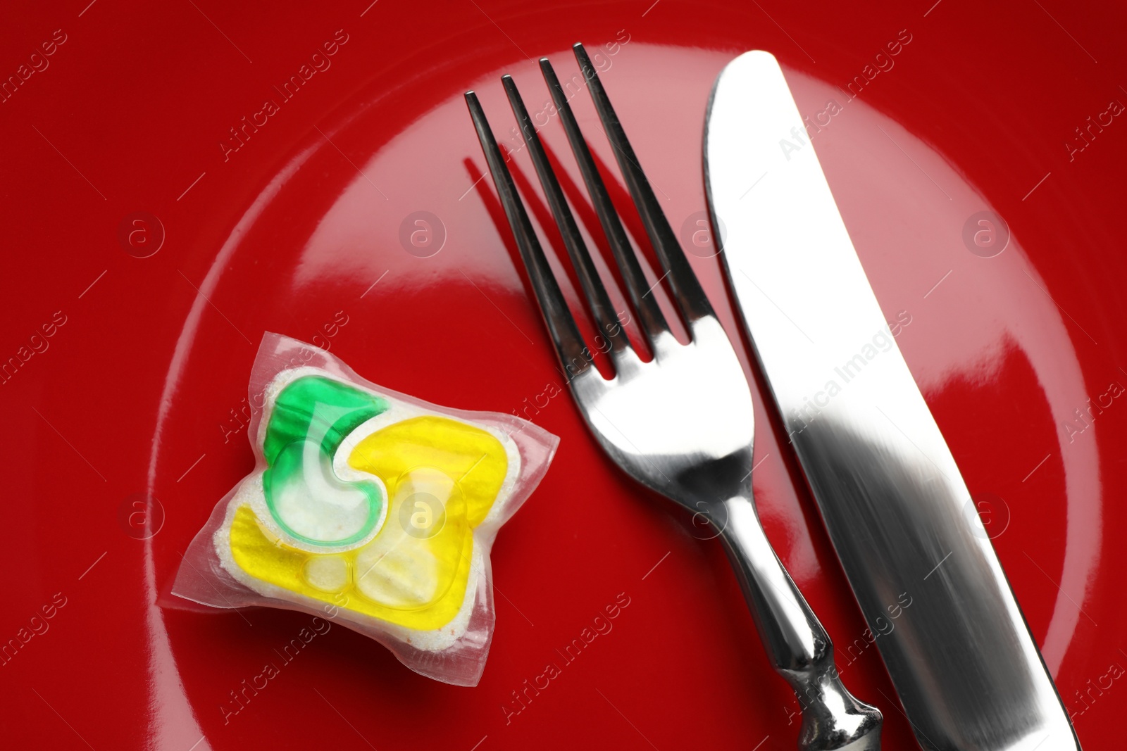 Photo of Red plate with cutlery and dishwasher detergent pod, top view