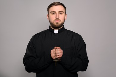 Priest in cassock with cross on grey background