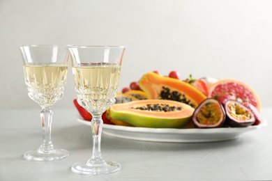 Delicious exotic fruits and glasses of wine on light grey table