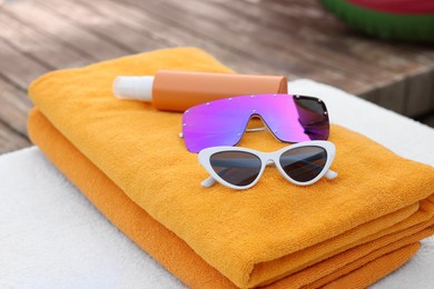 Beach towels, sunglasses and sunscreen on sunbed at resort, closeup