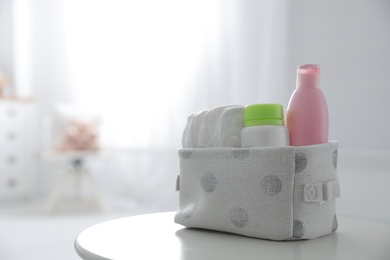 Basket with diapers and bottles on white table in baby room. Space for text