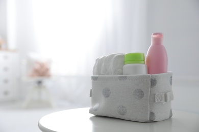 Photo of Basket with diapers and bottles on white table in baby room. Space for text