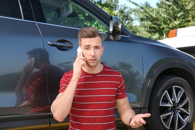 Photo of Man talking on phone near broken car and tow truck outdoors