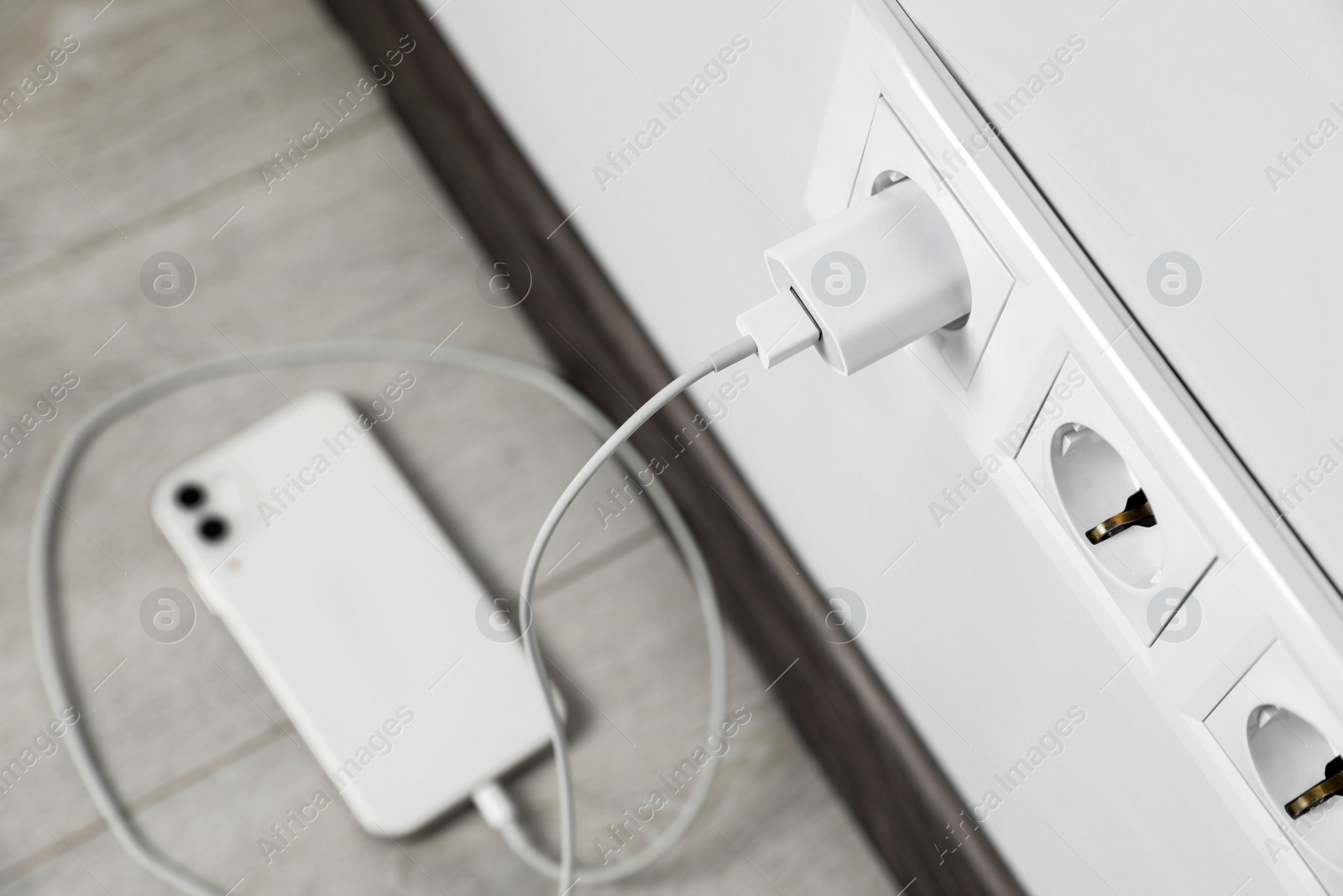 Photo of Modern smartphone charging from electric socket indoors, above view