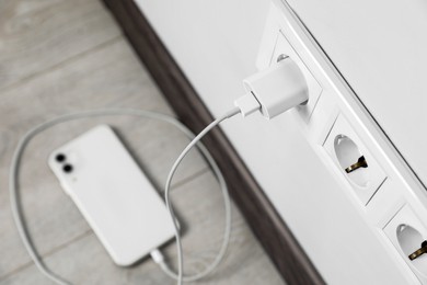 Modern smartphone charging from electric socket indoors, above view