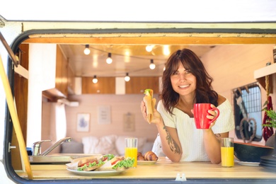 Photo of Young woman having breakfast in trailer, view from outside. Camping vacation