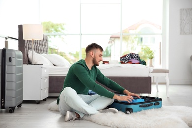Young man packing suitcase for summer journey at home
