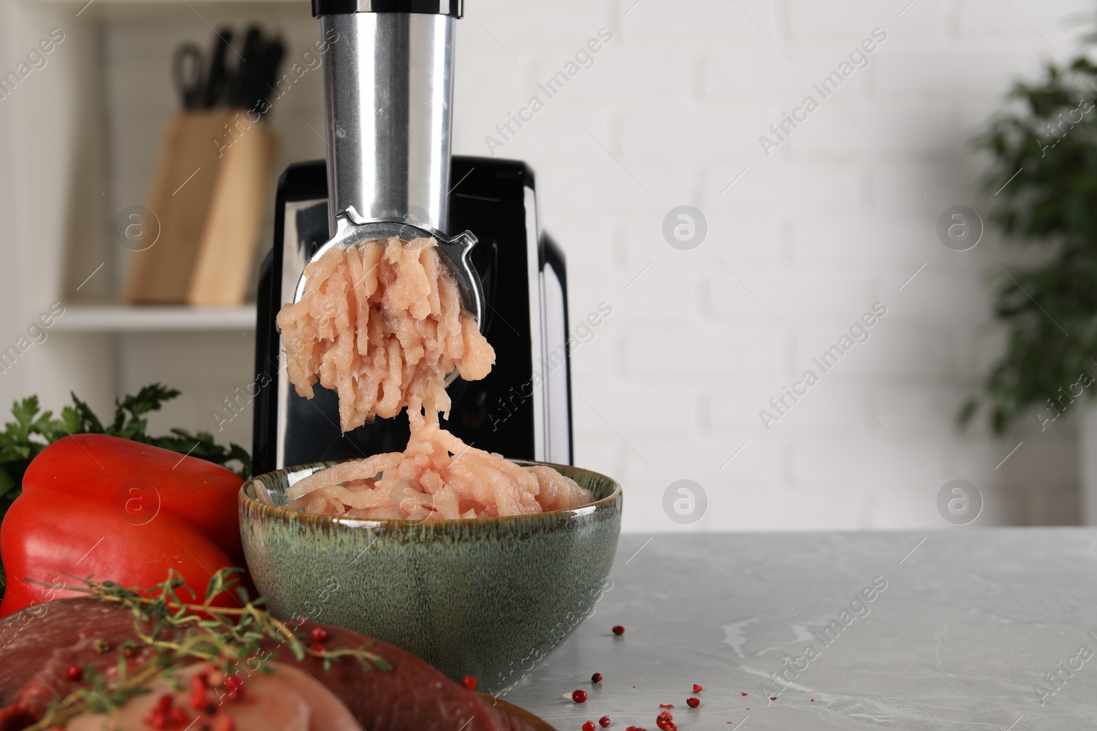 Photo of Electric meat grinder with chicken mince and products on grey marble table indoors. Space for text