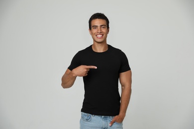 Handsome young African-American man in blank t-shirt on light background. Space for design