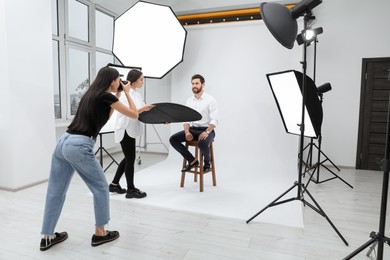 Photo of Professional photographer and assistant working with handsome model in modern photo studio