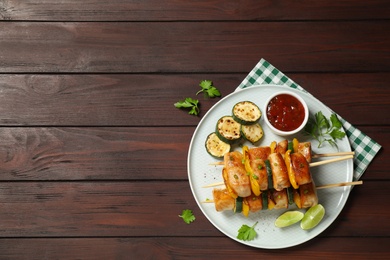 Photo of Delicious chicken shish kebabs with vegetables and sauce on wooden table, flat lay. Space for text