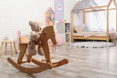 Teddy bear on wooden rocking horse in child's room, space for text. Interior design