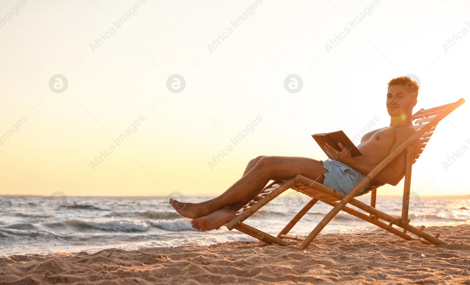 Photo of Young man reading book in deck chair on beach