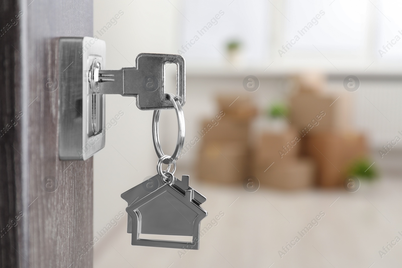 Photo of Mortgage and real estate. Open door with key and house shaped keychain against blurred background, space for text