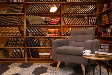 Photo of Cozy home library interior with comfortable armchair and collection of vintage books on shelves