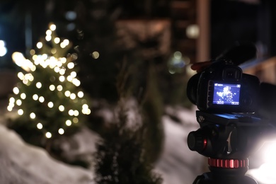 Photo of fir tree with Christmas lights on professional camera screen outdoors