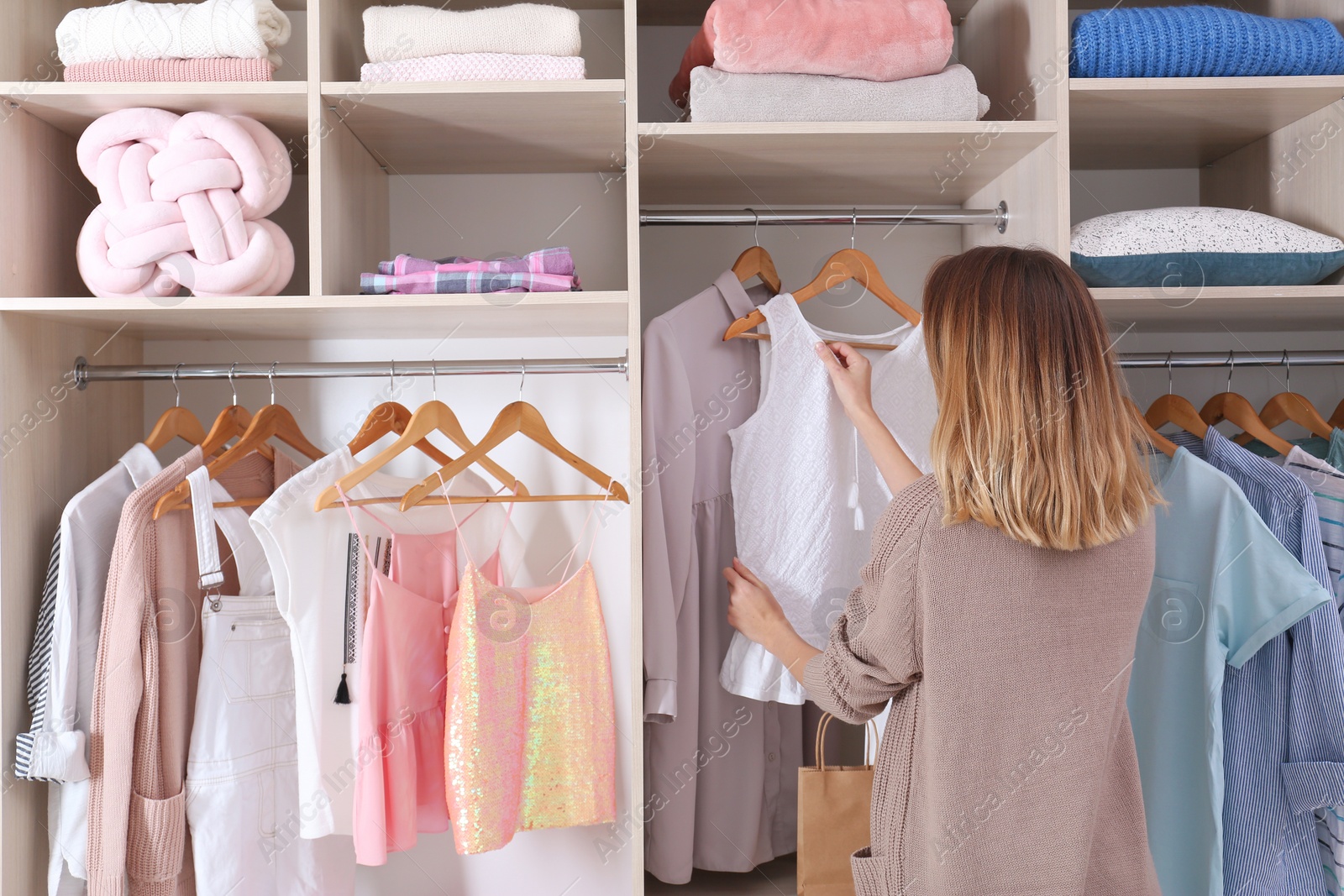 Photo of Woman choosing outfit from large wardrobe closet with stylish clothes and home stuff