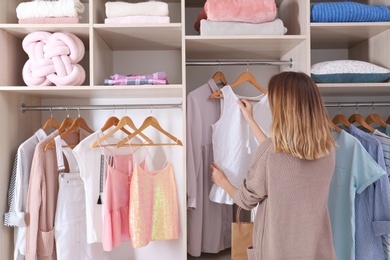 Woman choosing outfit from large wardrobe closet with stylish clothes and home stuff