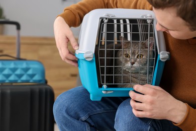 Travel with pet. Man holding carrier with cute cat indoors, closeup. Space for text