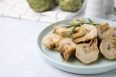 Photo of Plate with pickled artichokes and rosemary on white tiled table, closeup