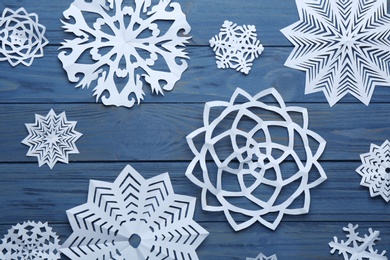 Flat lay composition with paper snowflakes on blue wooden background. Winter season