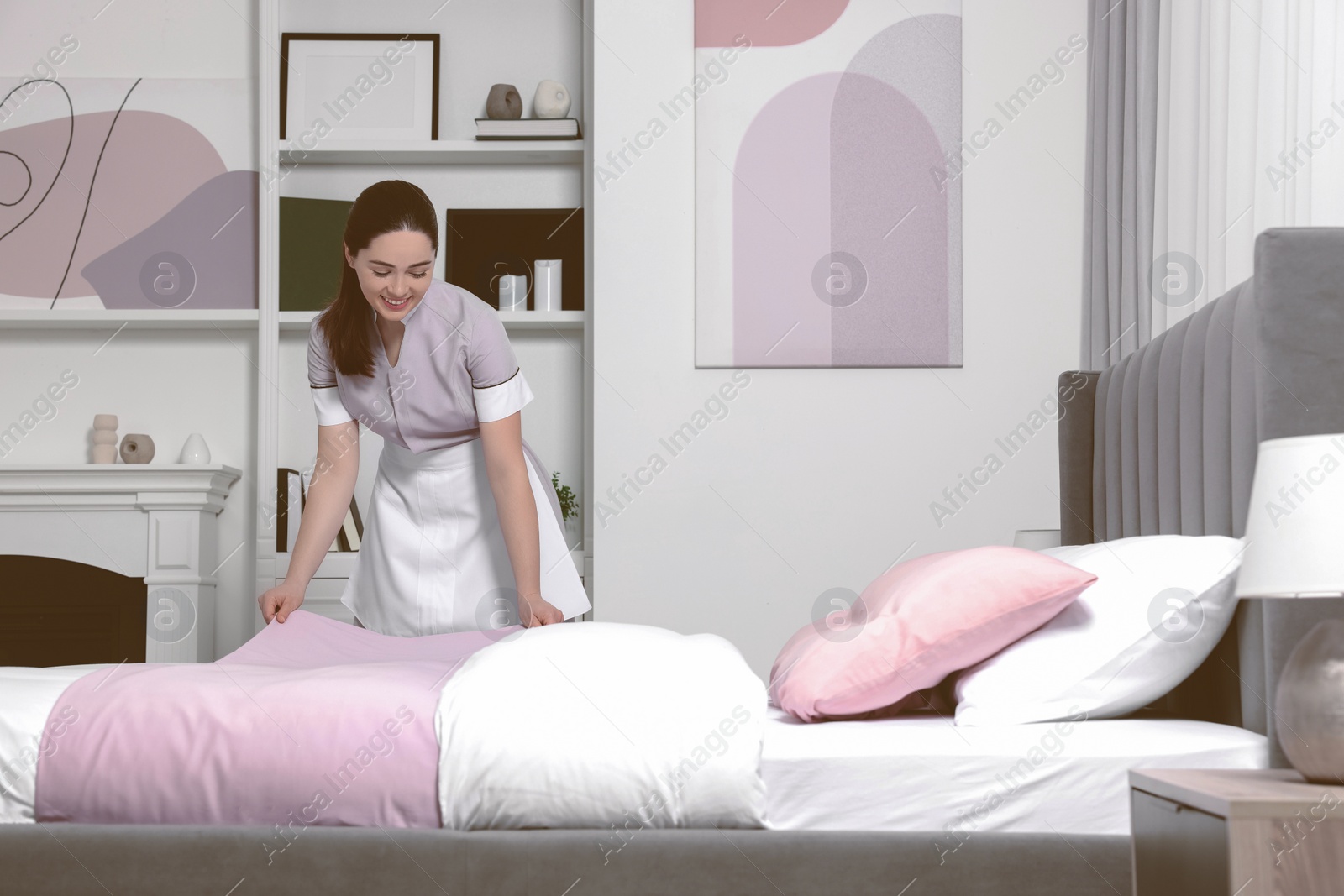 Photo of Young maid making bed in hotel room