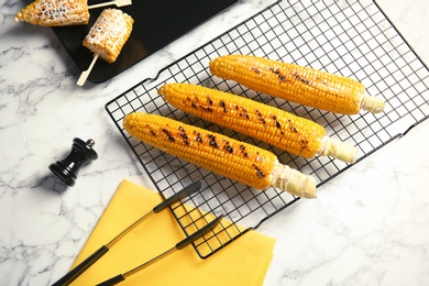 Photo of Cooling rack with grilled corn cobs on marble background, top view