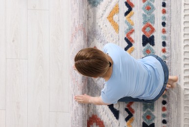 Photo of Woman unrolling carpet with beautiful pattern on floor in room, top view. Space for text