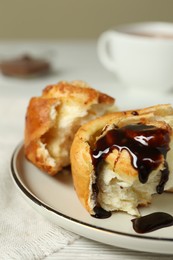 Delicious bun with chocolate sauce on white table, closeup