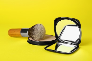 Photo of Stylish cosmetic pocket mirror, blusher and brush on yellow background