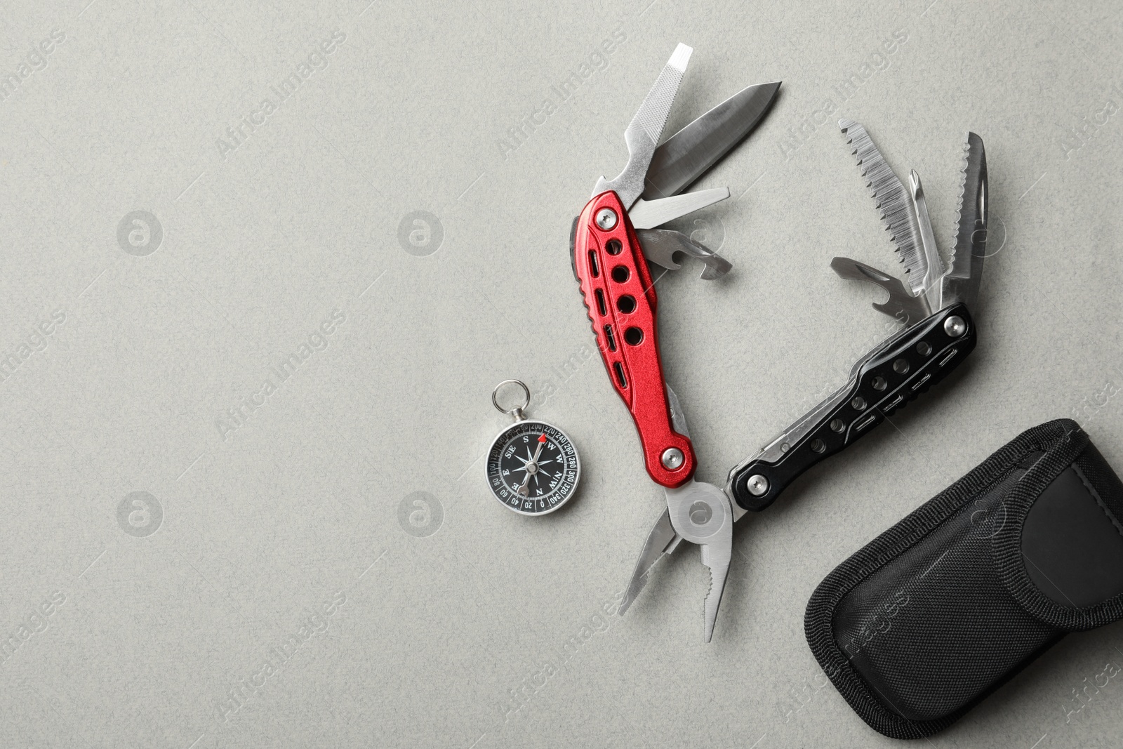 Photo of Compact portable multitool, case and compass on light grey background, flat lay. Space for text