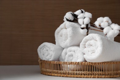Photo of Rolled soft towels and cotton branch on white table indoors, space for text