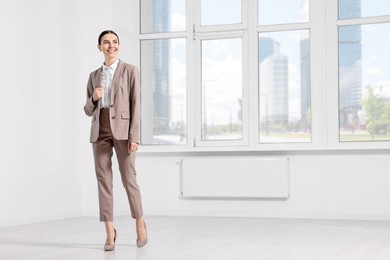 Photo of Beautiful real estate agent wearing nice suit in empty room, space for text