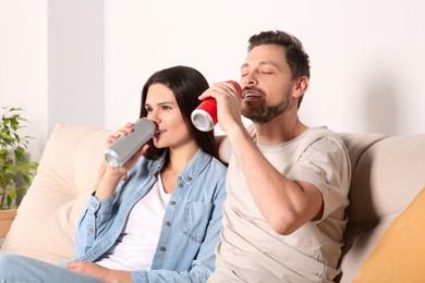Photo of Happy couple drinking beverages on sofa indoors