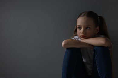 Sad girl sitting near dark grey background, space for text