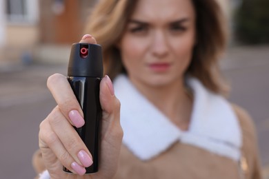 Young woman using pepper spray outdoors, focus on hand