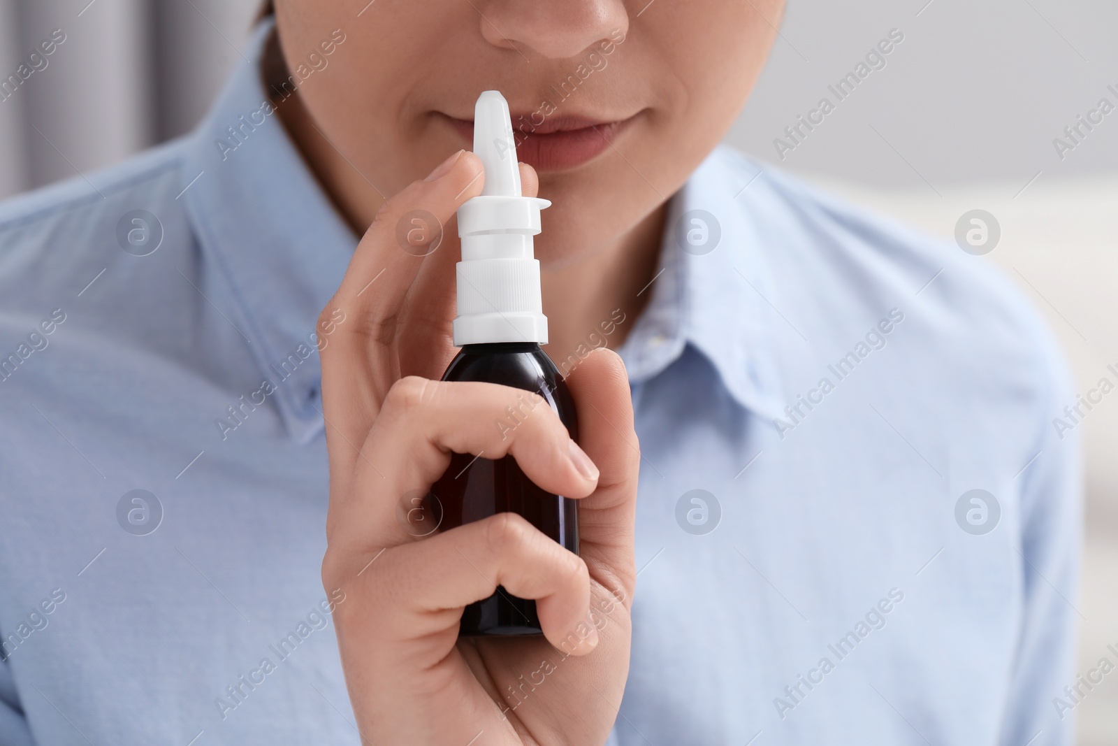 Photo of Woman using nasal spray on blurred background, closeup