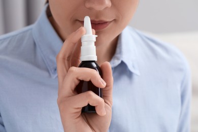 Photo of Woman using nasal spray on blurred background, closeup