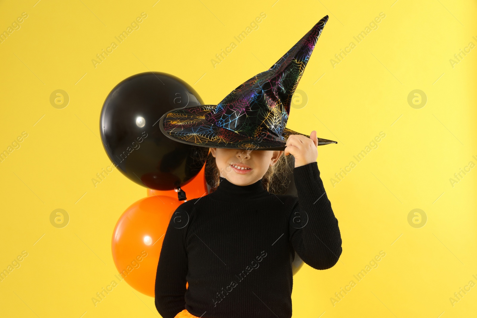 Photo of Cute little girl with balloons wearing Halloween costume on yellow background