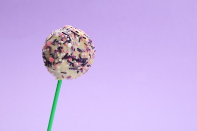 Photo of Delicious confectionery. Sweet cake pop decorated with sprinkles on light violet background, closeup. Space for text