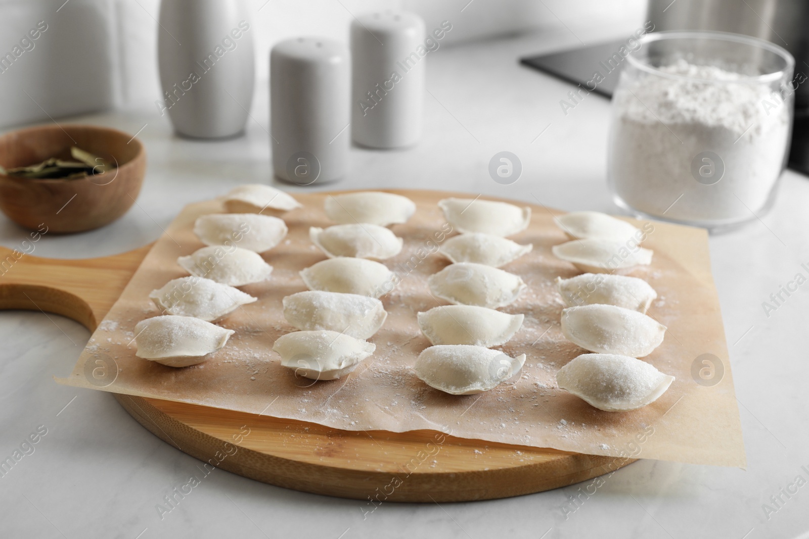 Photo of Fresh uncooked dumplings and flour on white table