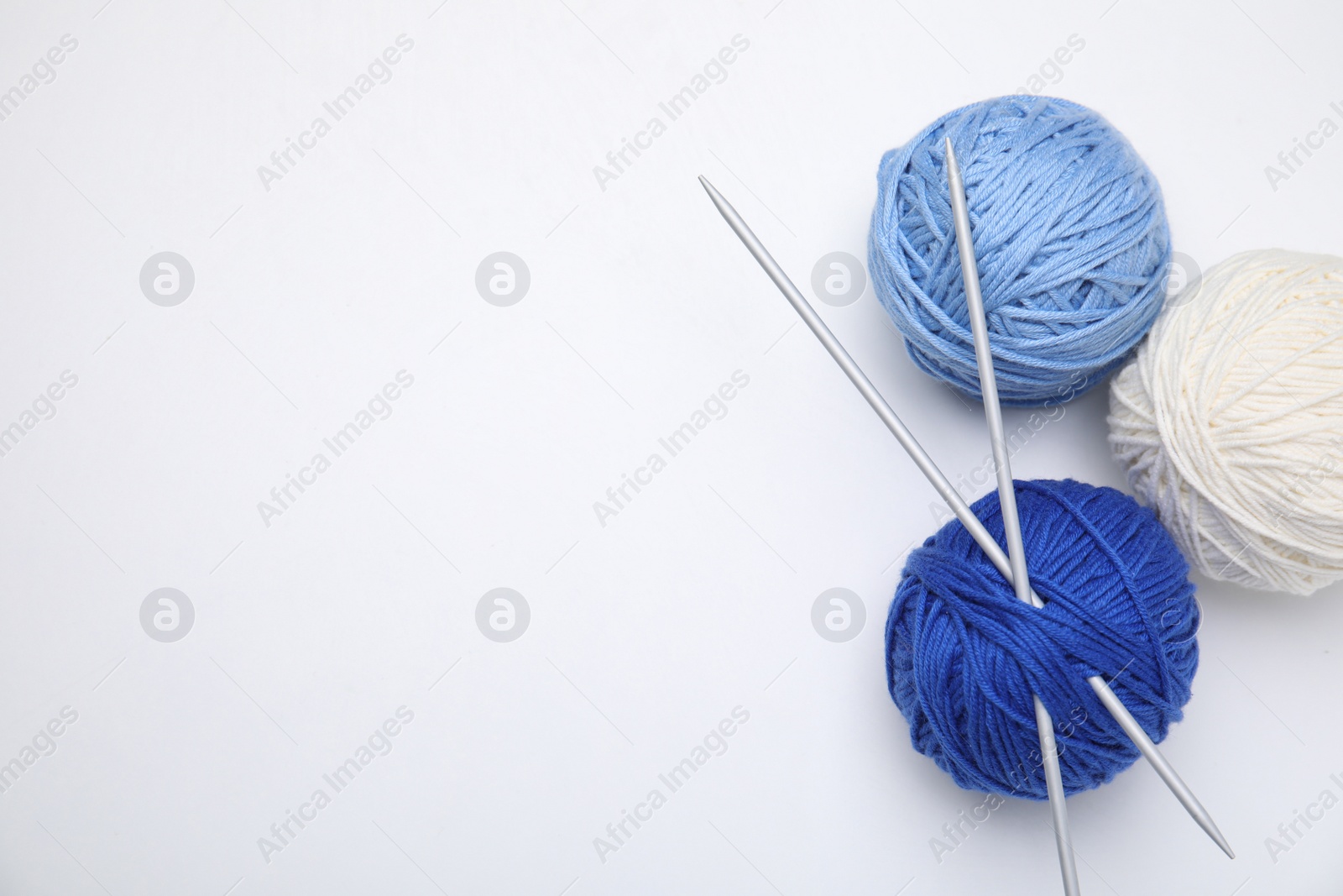 Photo of Soft woolen yarns with knitting needles on white background, top view