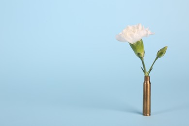 Photo of Bullet cartridge case and beautiful carnation flower on light blue background, space for text