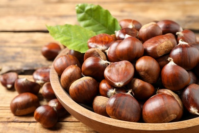 Photo of Fresh sweet edible chestnuts in bowl on table, closeup